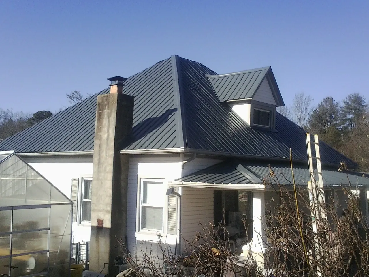 Dark blue standing seam metal roof on a white farmhouse with dormer — Slate & Tile Roof Repair by Roofing Brothers in Thaxton