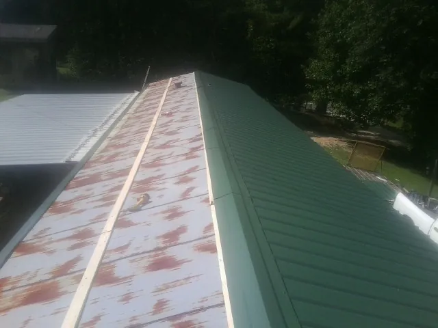 Old rusted panels beside newly installed green metal roofing — Wind Damage Roof Repair by Roofing Brothers in Thaxton