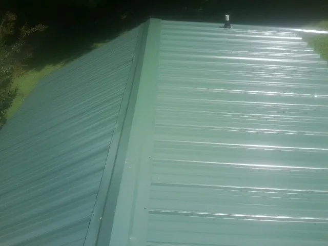New green metal panels meeting at the ridge of a roof — Flat Roof Repair work by our crew in Thaxton