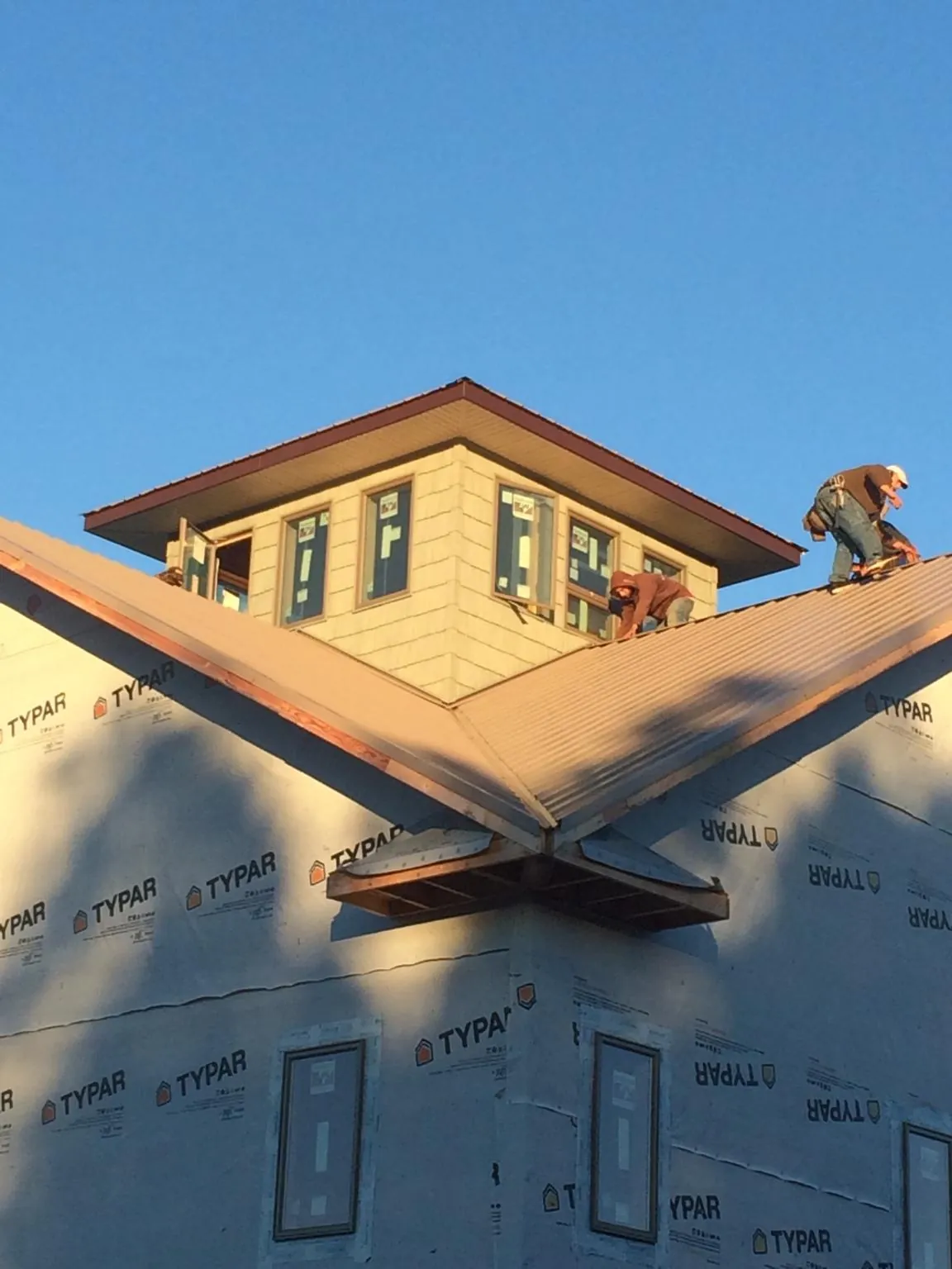 Roofers working around a rooftop cupola on a new metal roof at sunset — Roof Waterproofing in Thaxton by Roofing Brothers